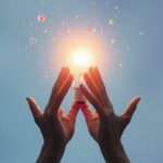 Person reaching for glowing light bulb symbolizing knowledge.